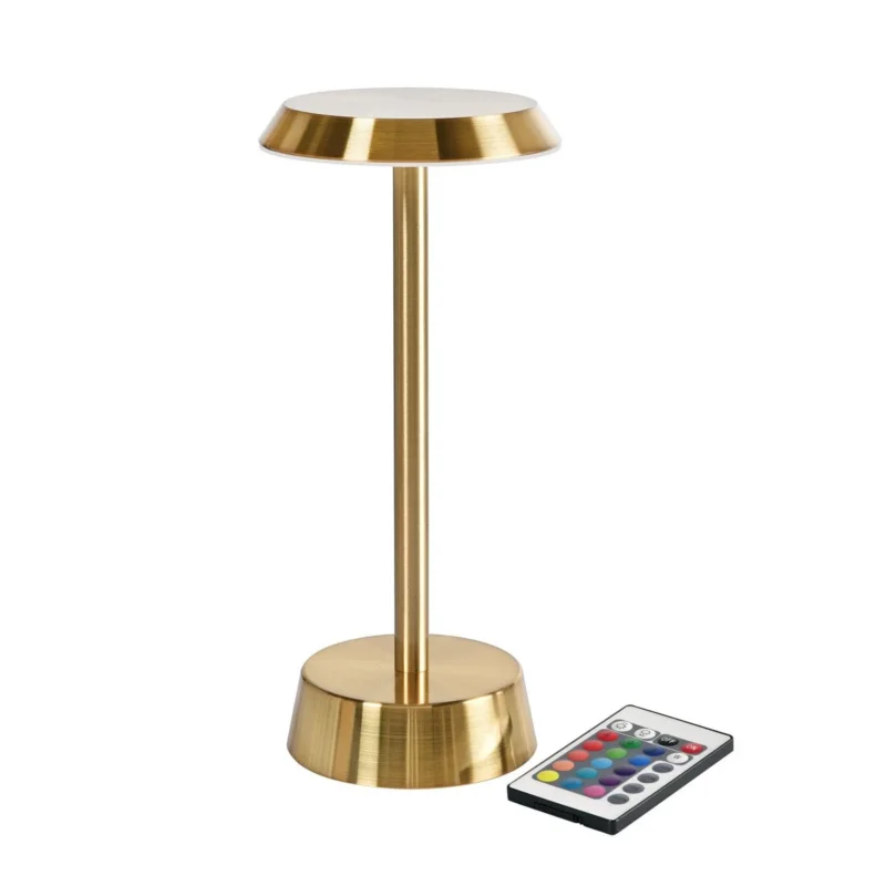 Die LED-Lampe kabellos NOUR in Messing von Duni GmbH mit modernem Design und rundem Fuß ergänzt stilvoll die elegante Messingvase und den bunten Fernbedienungsknopf auf dem Tisch.