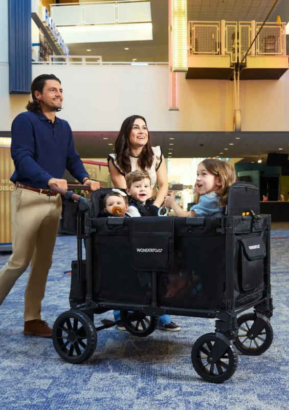 Eine lächelnde Familie mit drei Kindern nutzt den WonderFold W4 Luxe Pro Kinderwagen 4-Sitzer Jet Schwarz in einem modern gestalteten Innenbereich.