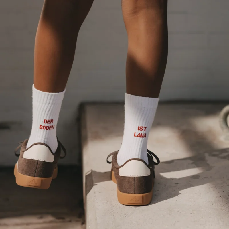 Weiße Kindersocken mit rotem Schriftzug „Der Boden“ und „Lava“ am Bündchen